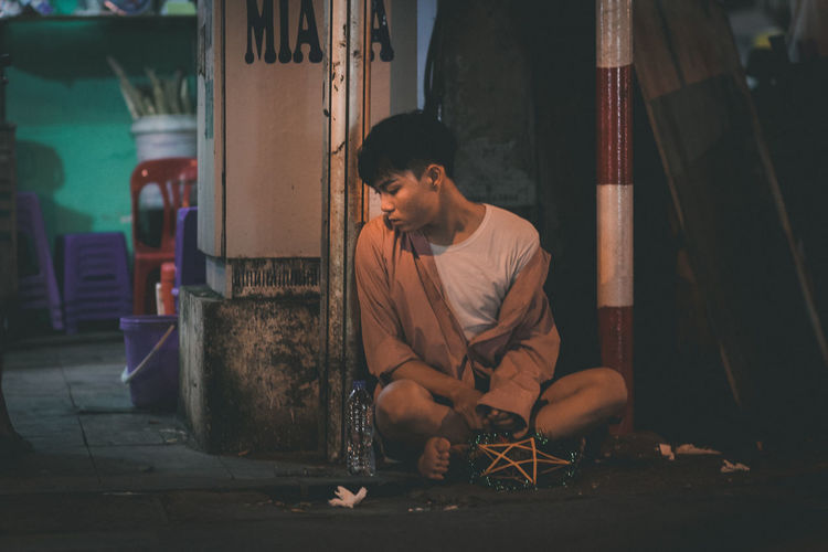 Full length of beggar man sitting on sidewalk at night