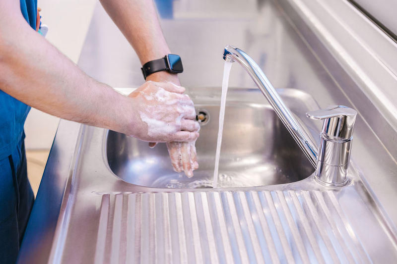 Doctor washing hands with water in sink at hospital