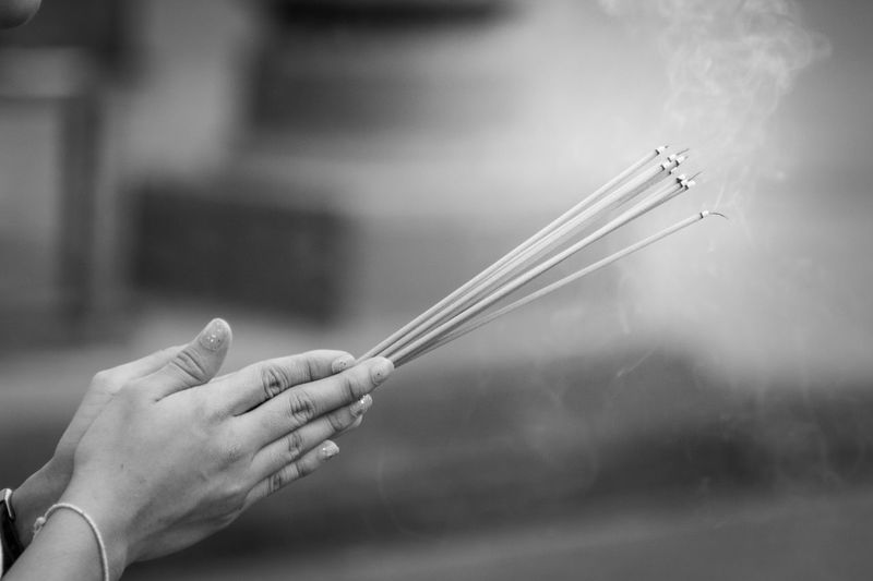 Cropped hands of woman holding lit incense sticks while praying at temple