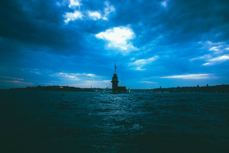 View of lighthouse in sea against cloudy sky