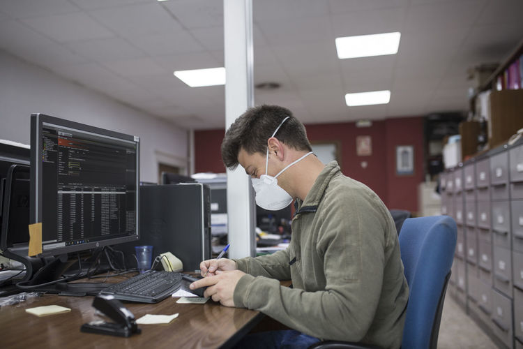 Side view of man working at the office with mask