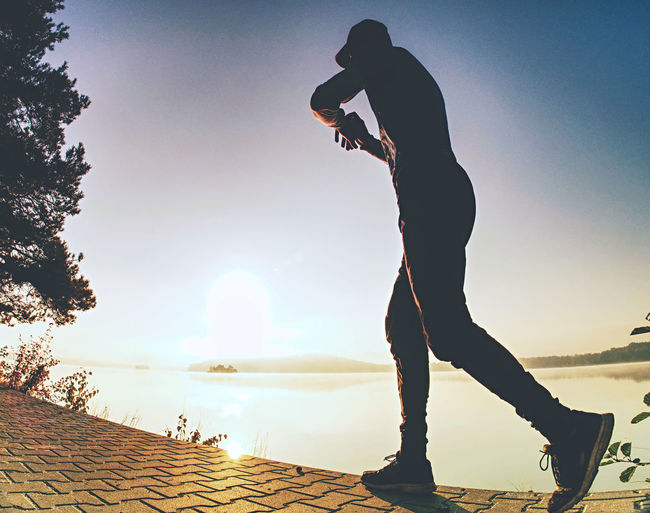 Low angle view of man skateboarding on lake against sky during sunset