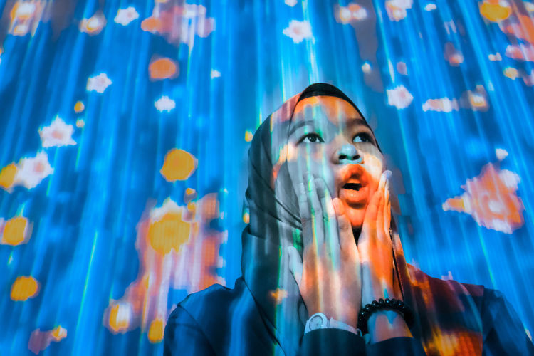 Close-up of surprised girl looking away with illuminated multi colored lights