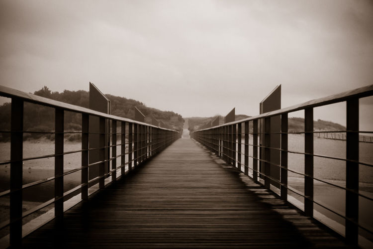 Footbridge amidst water against sky