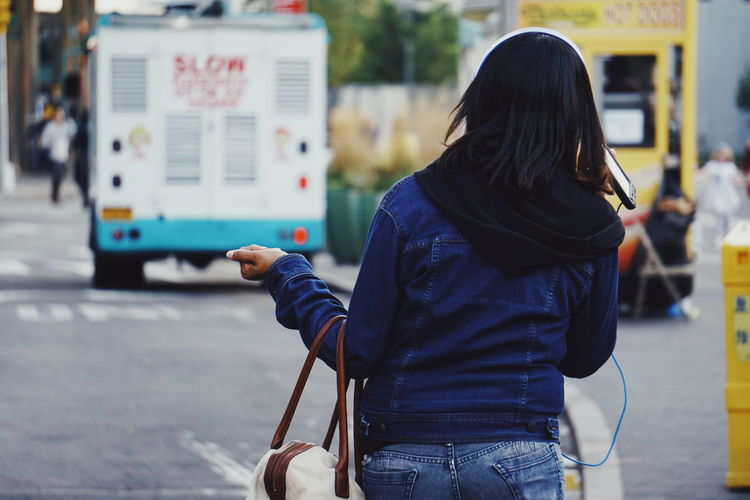 Rear view of woman using mobile phone while walking on street