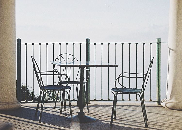 Chairs on railing by sea against sky