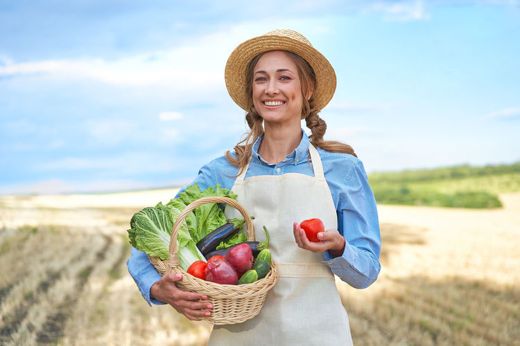 Portrait of smiling woman holding fruits in basket at farm
