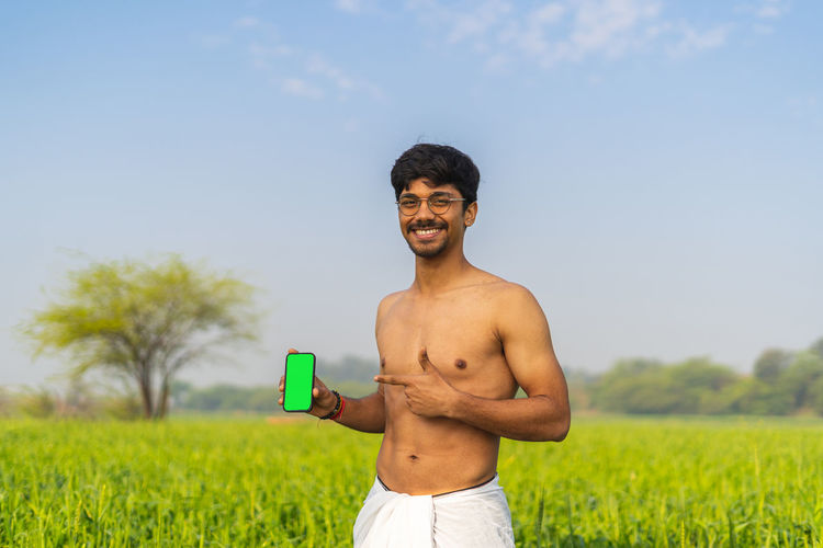 Portrait of young man drinking water while standing on field