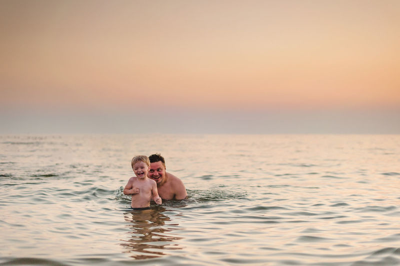 PORTRAIT OF COUPLE SWIMMING IN SEA AT SUNSET