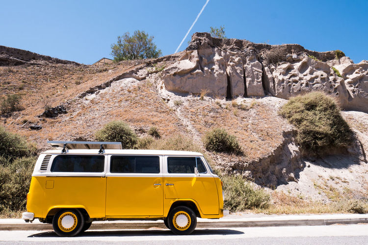 Yellow vintage car on road by rock formation against sky