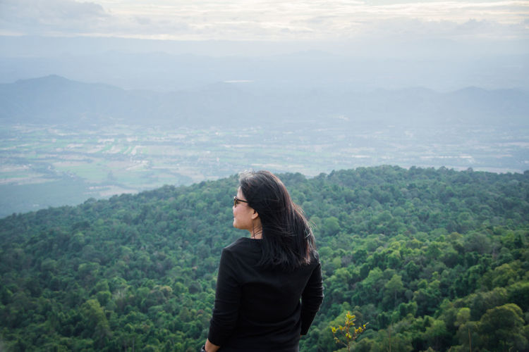 Rear view of woman looking away while standing against mountain landscape