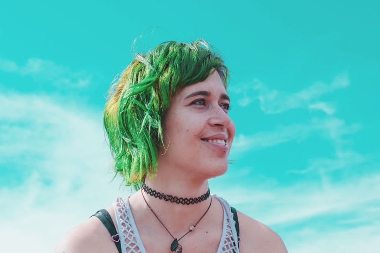 Close-up of beautiful woman with green dyed hair against sky