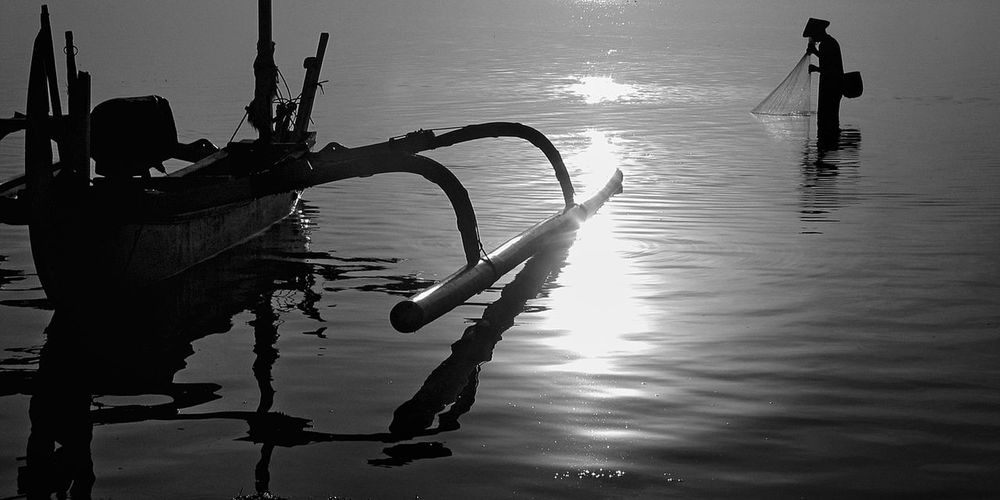 Silhouette men fishing in lake against sky
