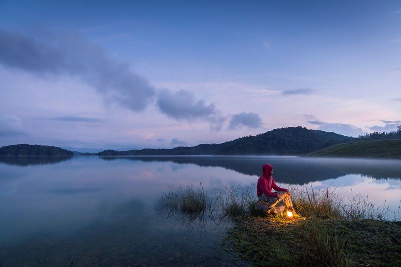 Man sitting on lakeshore against sky