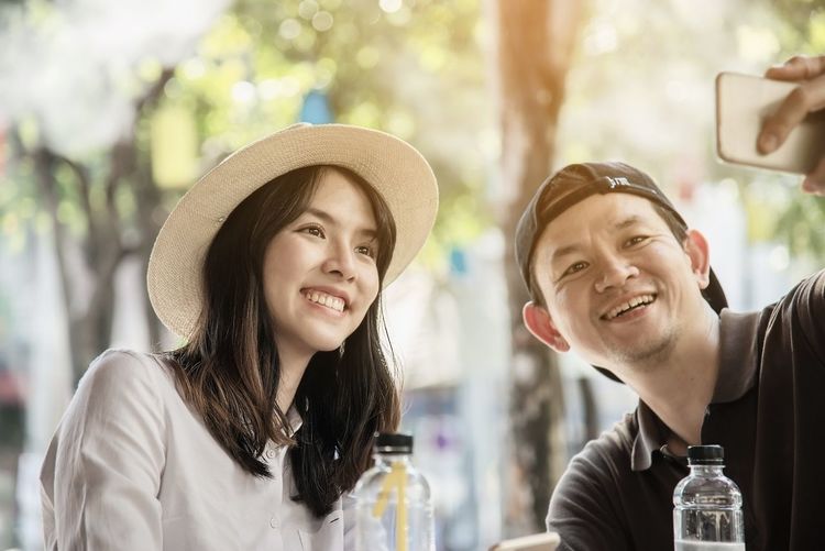 Smiling man taking selfie with woman while sitting at outdoor cafe