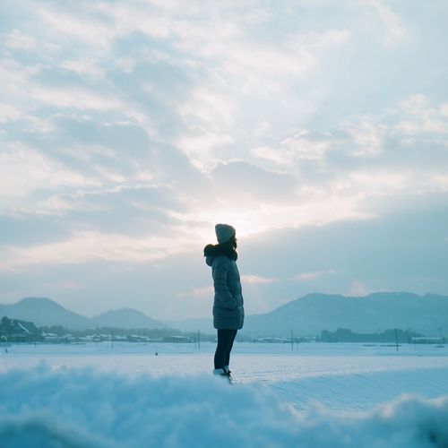 Woman standing on snow covered field against sky