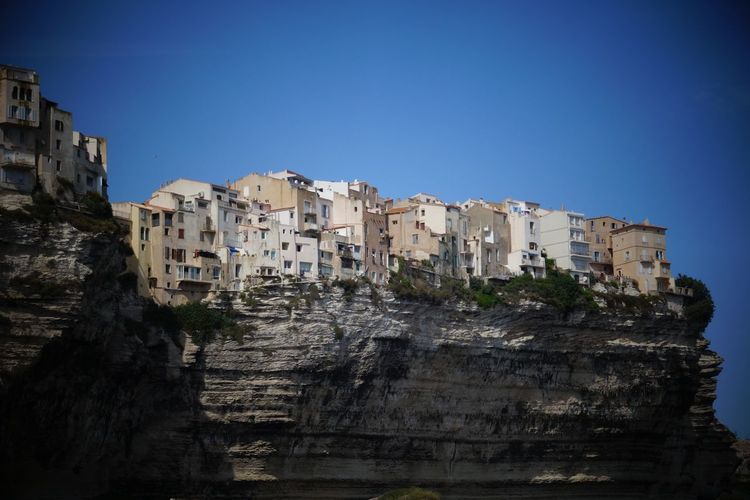 Low angle view of buildings over cliff  against blue sky