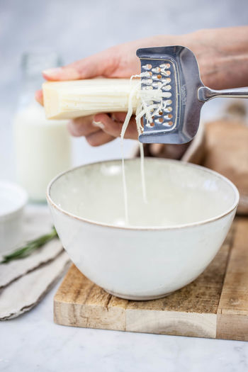 Cropped hands grating cheese in bowl on table