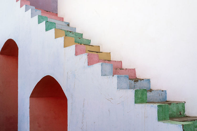 White weathered house with painted wall and multicolored shabby steps located on street against cloudless sky in city of egypt