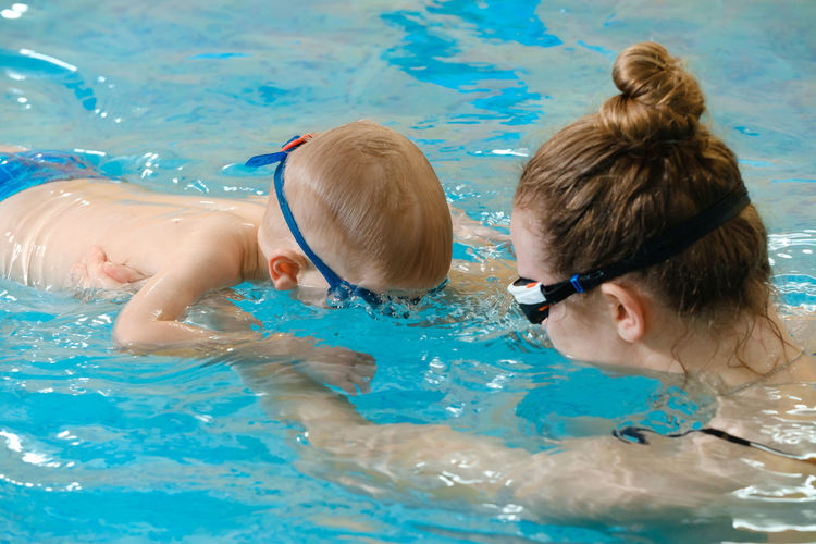 Toddler child learning to dive in indoor swimming pool with teacher.