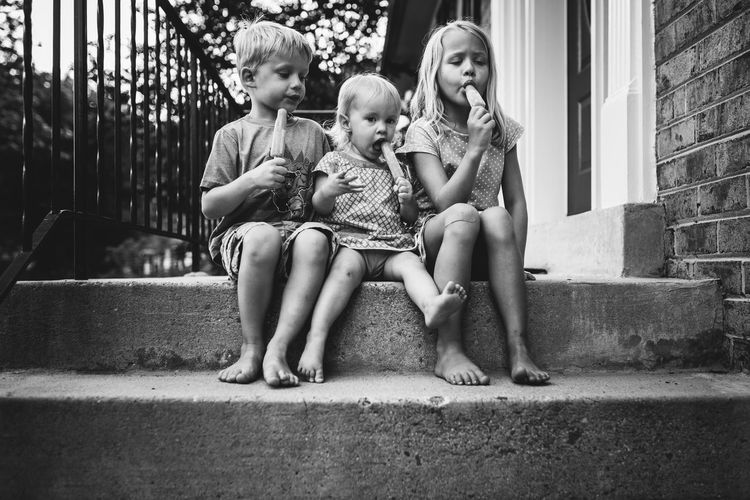 Full length of siblings eating popsicle while sitting on steps