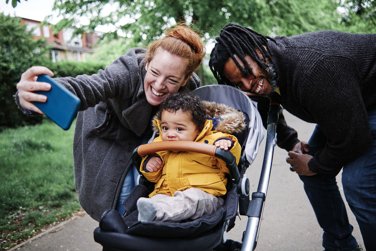 Cheerful parents taking selfie with son in stroller at park