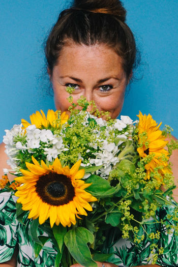 Close-up portrait of mid adult woman holding bouquet against blue background