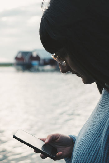 Woman wearing eyeglasses using smart phone by lake