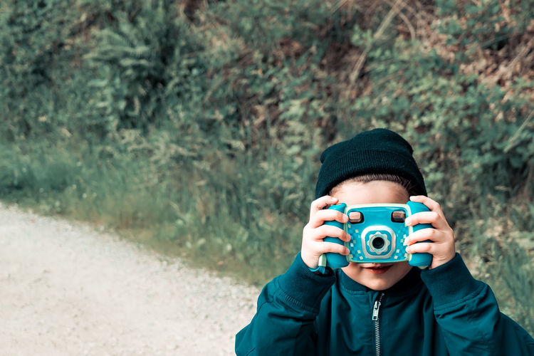 Boy with face covered by toy camera standing on footpath