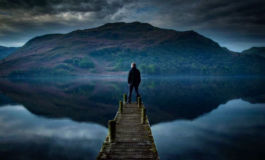 Rear view of man standing on pier over lake against mountain