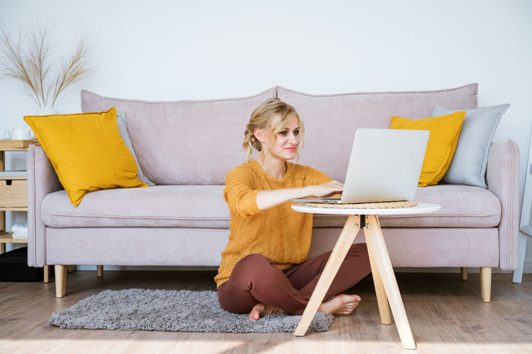 Attractive woman sitting on floor and sofa using laptop chatting while working