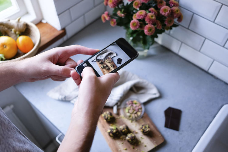 Cropped image of man photographing food through mobile phone at kitchen counter