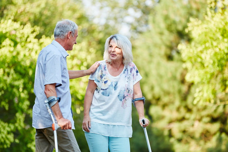 Senior couple with walking canes standing against trees at park