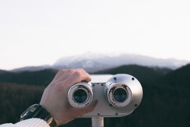 Cropped image of hand holding coin-operated binoculars against mountain