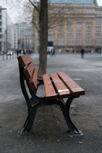 Empty bench on street by buildings in city