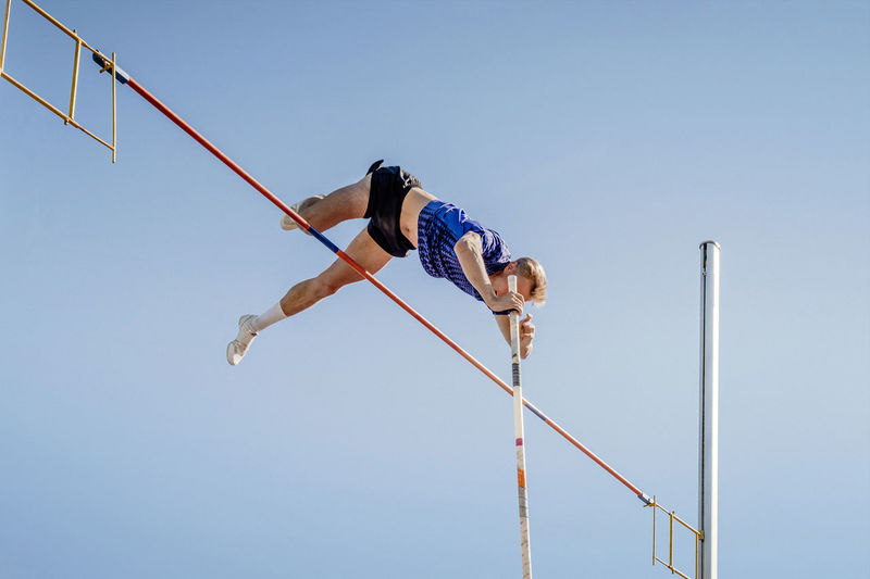 Male athlete pole vault on blue sky background