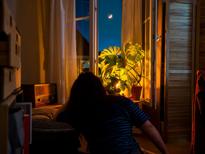 Rear view of woman sitting by window at home