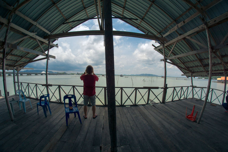 Rear view of man standing in gazebo over sea against cloudy sky