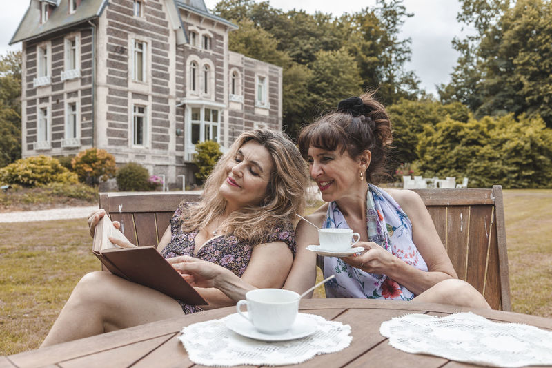 Couple of mature friendly women on vacation drinking tea and reading a book outdoors