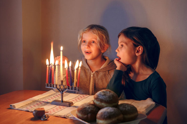 Girls friends lighting candles on menorah for traditional winter jewish hanukkah holiday at home