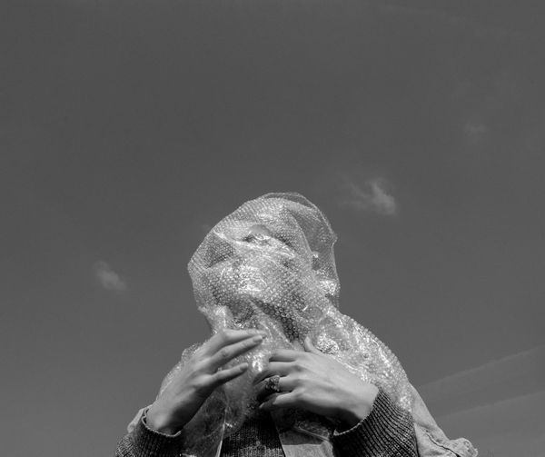 Low angle view of woman covered in bubble wrap standing against sky