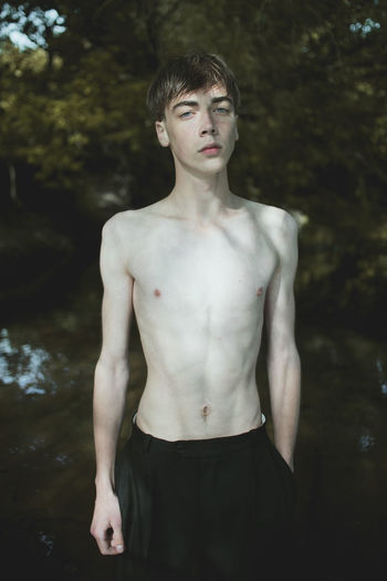 Portrait of shirtless man standing by lake