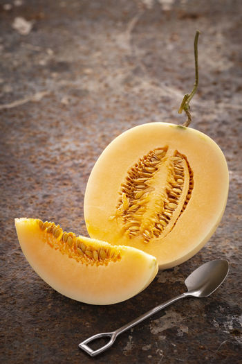 Sliced yellow cantaloupe melon with dessert spoon on rusty texture background