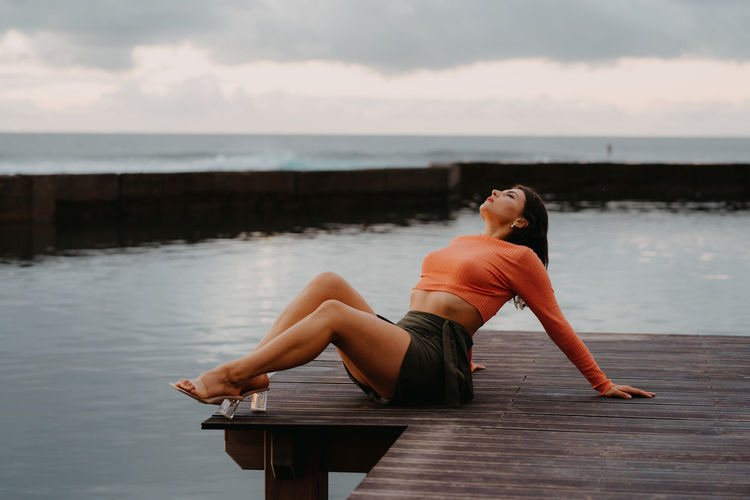 Woman sitting on pier over sea against sky