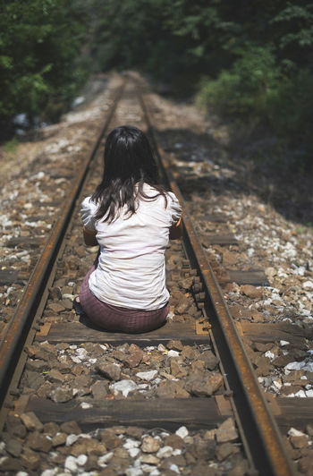 Rear view of woman sitting on railroad track