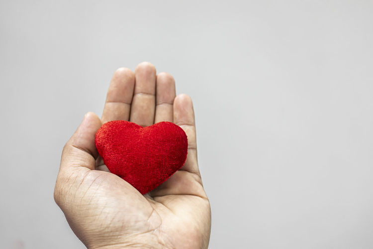 Close-up of hand holding heart shape over white background