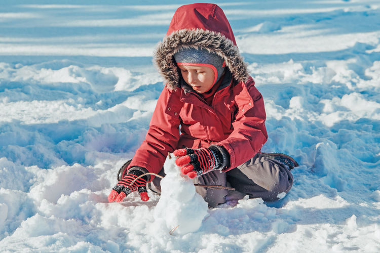 Girl child in warm clothes playing with snow in park outside. kids outdoor seasonal activity.