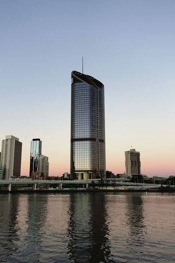 Modern buildings by river against sky during sunset