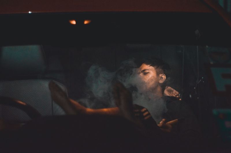 Man exhaling smoke in car at night