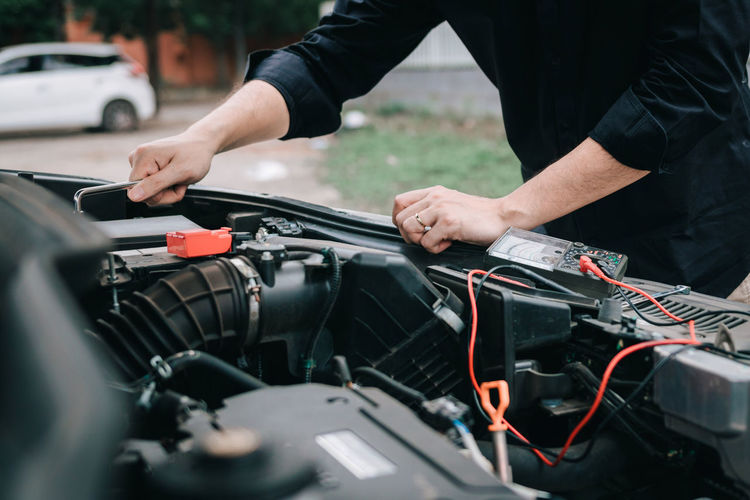 Midsection of man repairing car engine on roadside